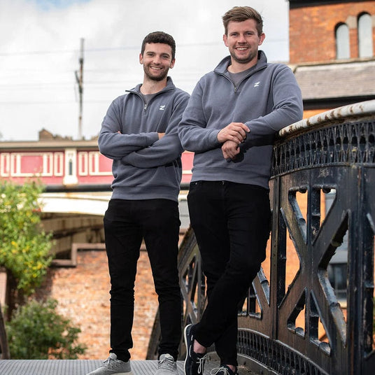 Two men wearing matching gray sweatshirts standing on a bridge.